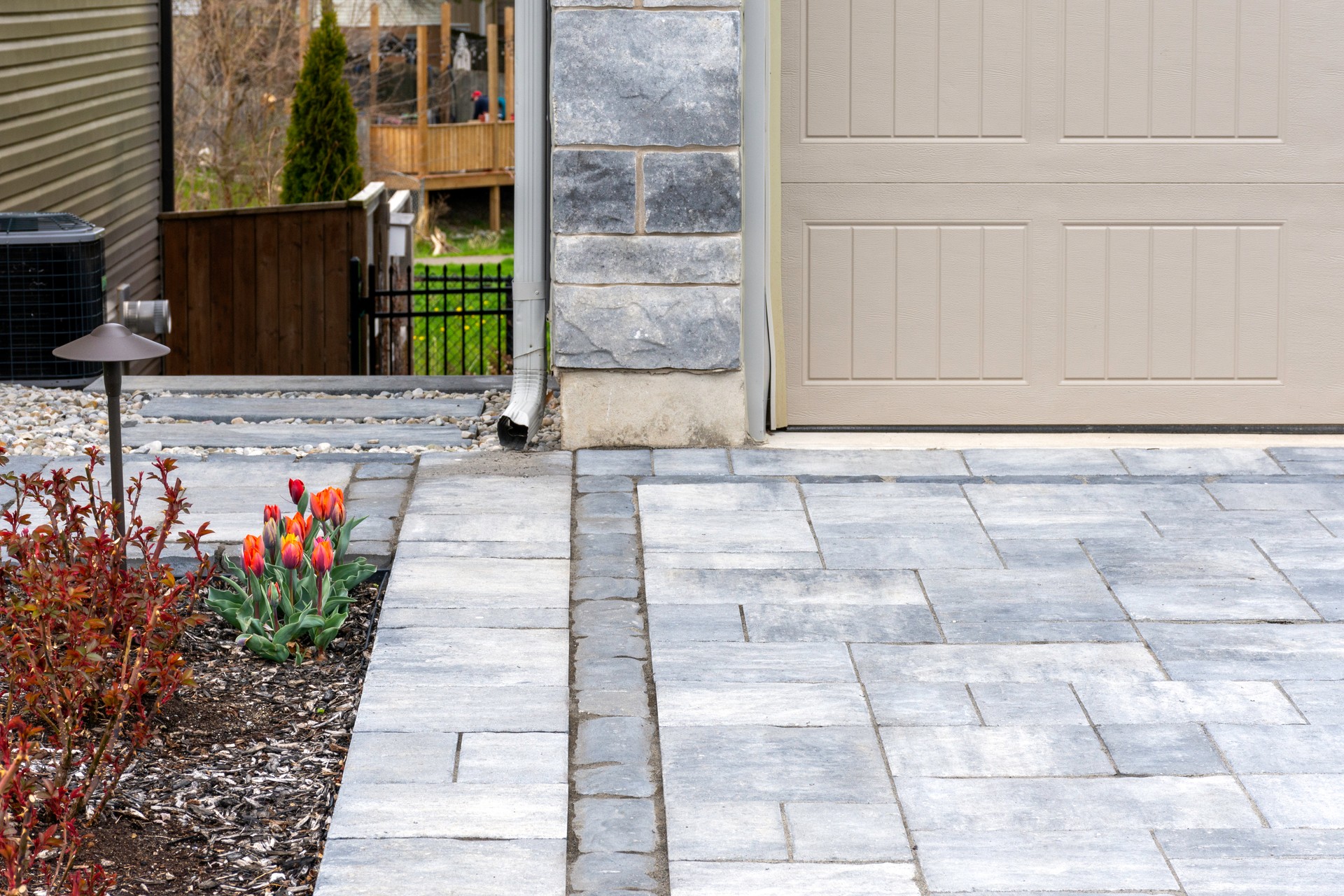 Closeup detail of modern landscaping shows residential driveway pavers with a contrasting dark band.